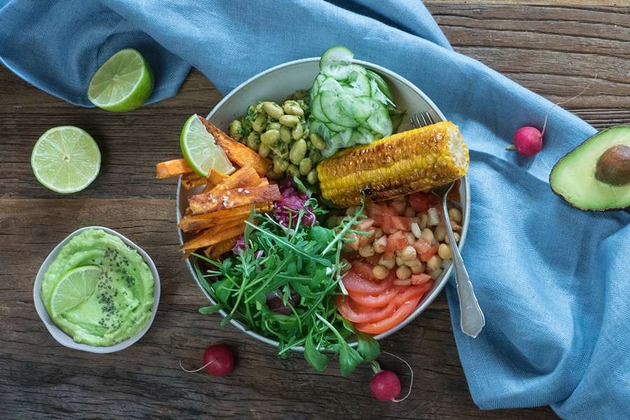 Bowl mit Kichererbsen, Pesto, Süßkartoffel-Pommes und Maiskolben