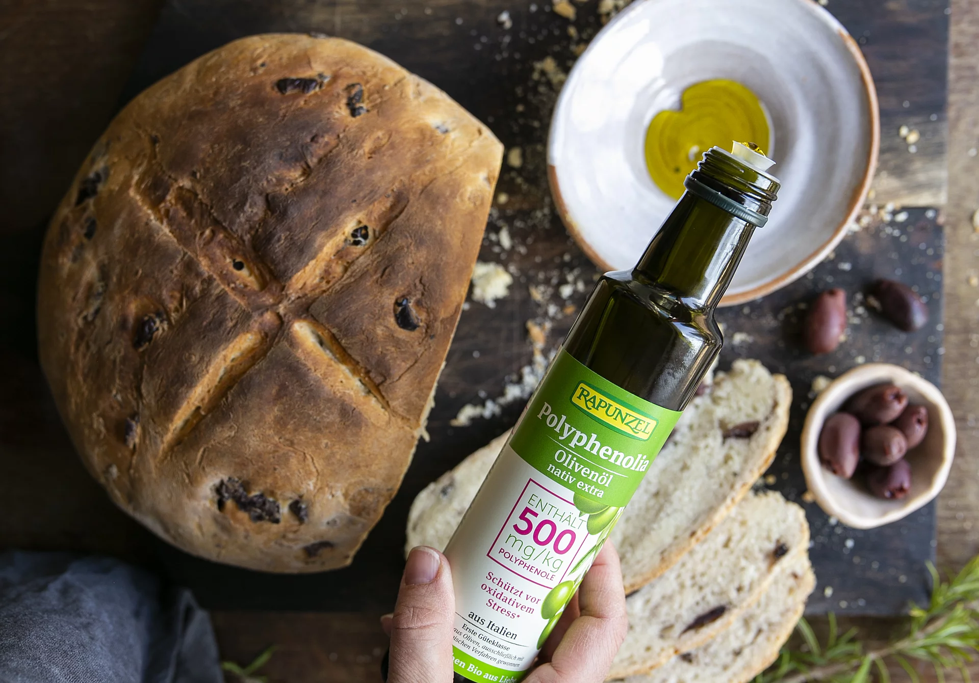 Rapunzel Polyphenolia – Bio-Olivenöl mit Steinofenbrot und Oliven. Steinofenbrot mit Olivenschälchen und Rapunzel Polyphenolia Bio-Olivenöl – mediterraner Genuss aus kontrolliert biologischem
