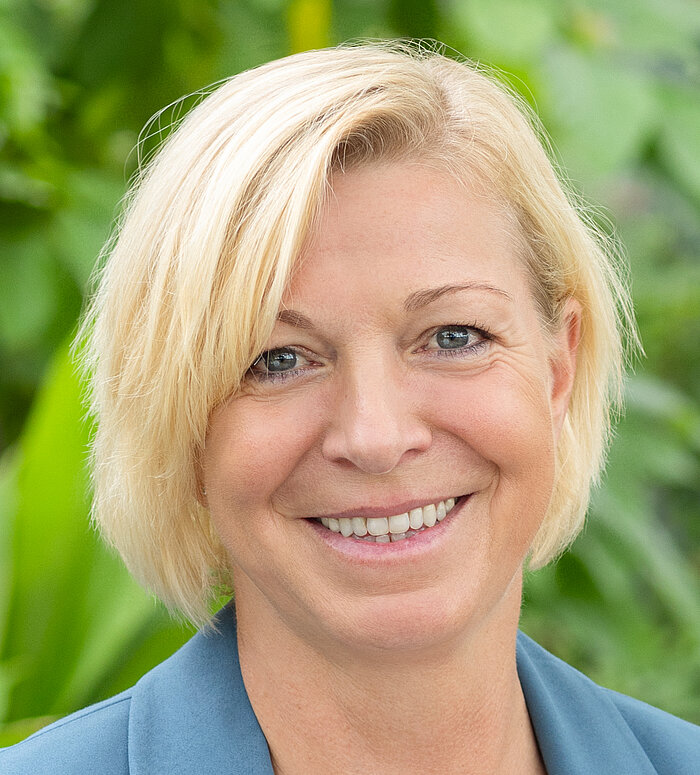 Rapunzel Mitarbeiterin steht vor blühender Pflanze.