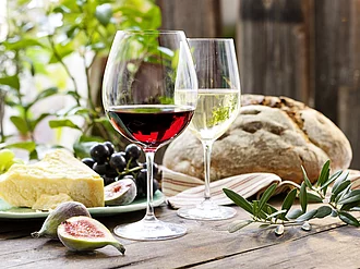 Gefülltes Rotweinglas vor Weißweinglas, daneben Käse und Brot.