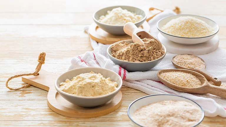 Verschiedene Spezialmehle in Schüsseln auf Tisch, sie bestehen aus Saaten, Hülsenfrüchten, Nüssen und Co.