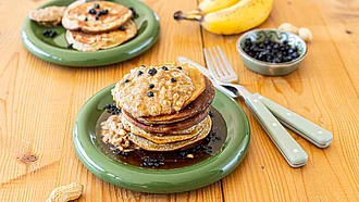 Mehrere Pancakes übereinandergeschichtet auf grünem Teller auf einem Tisch.