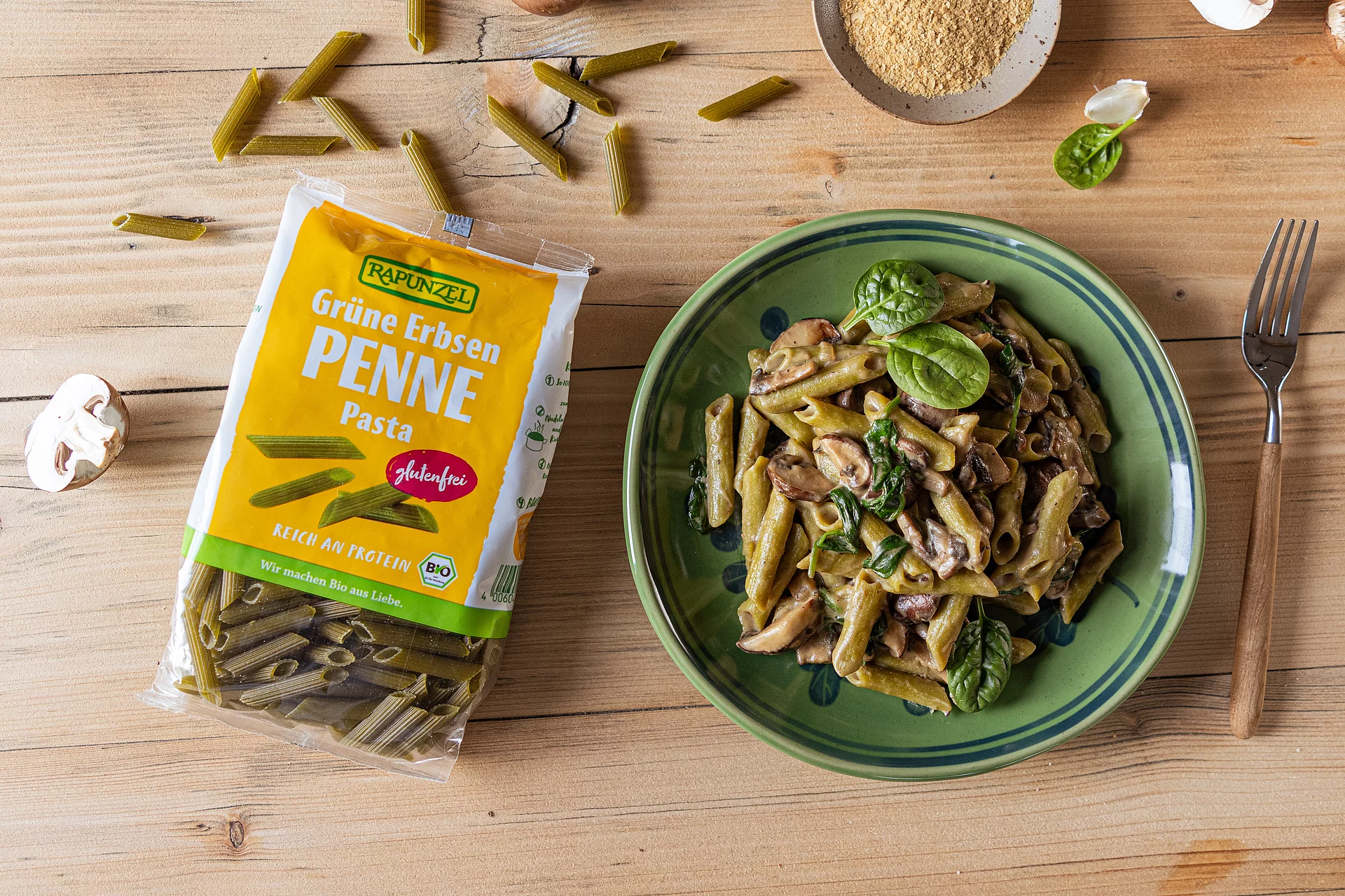 Grüne Erbsen Penne mit cremiger Pilzsauce in einer Schale serviert. Daneben liegt eine offene Packung der Grünen Erbsen Penne.