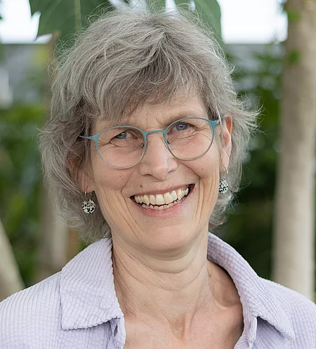 Porträt von Anke Malas, Mitarbeiterin im Rapunzel Kundenservice, lächelnd vor Pflanzen im Tropenhaus.