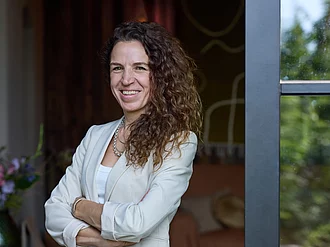 Rapunzel Geschäftsführerin Seraphine Wilhelm steht in einer schick-rustikalen Umgebung vor einem Bauernhof und lächelt in die Kamera