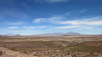Hochland mit brauner Erde und Berge im Hintergrund, blauer Himmel.