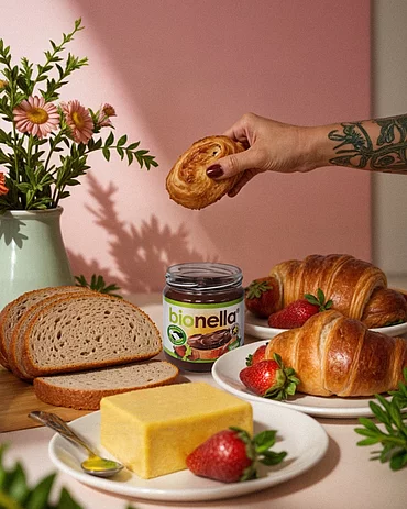 Gedeckter Tisch mit bionella, Butter, Brot, Croissants. In der Hand ein Croissants.