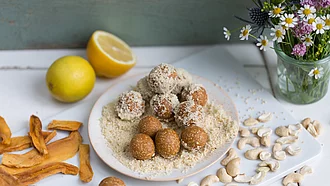 Fruchtkugeln aus Erdmandeln auf einem Teller, daneben die Zutaten Mango und Cashewkerne.