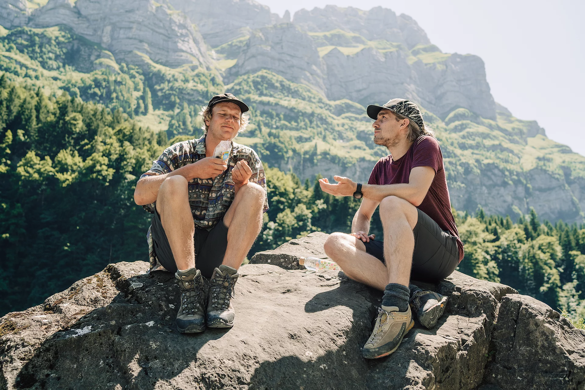 Zwei Wanderer haben sich zur Rast auf einem Großen Stein gesetzt, einer von ihnen hält eine Tüte salzige Snacks von Rapunzel in den Händen.