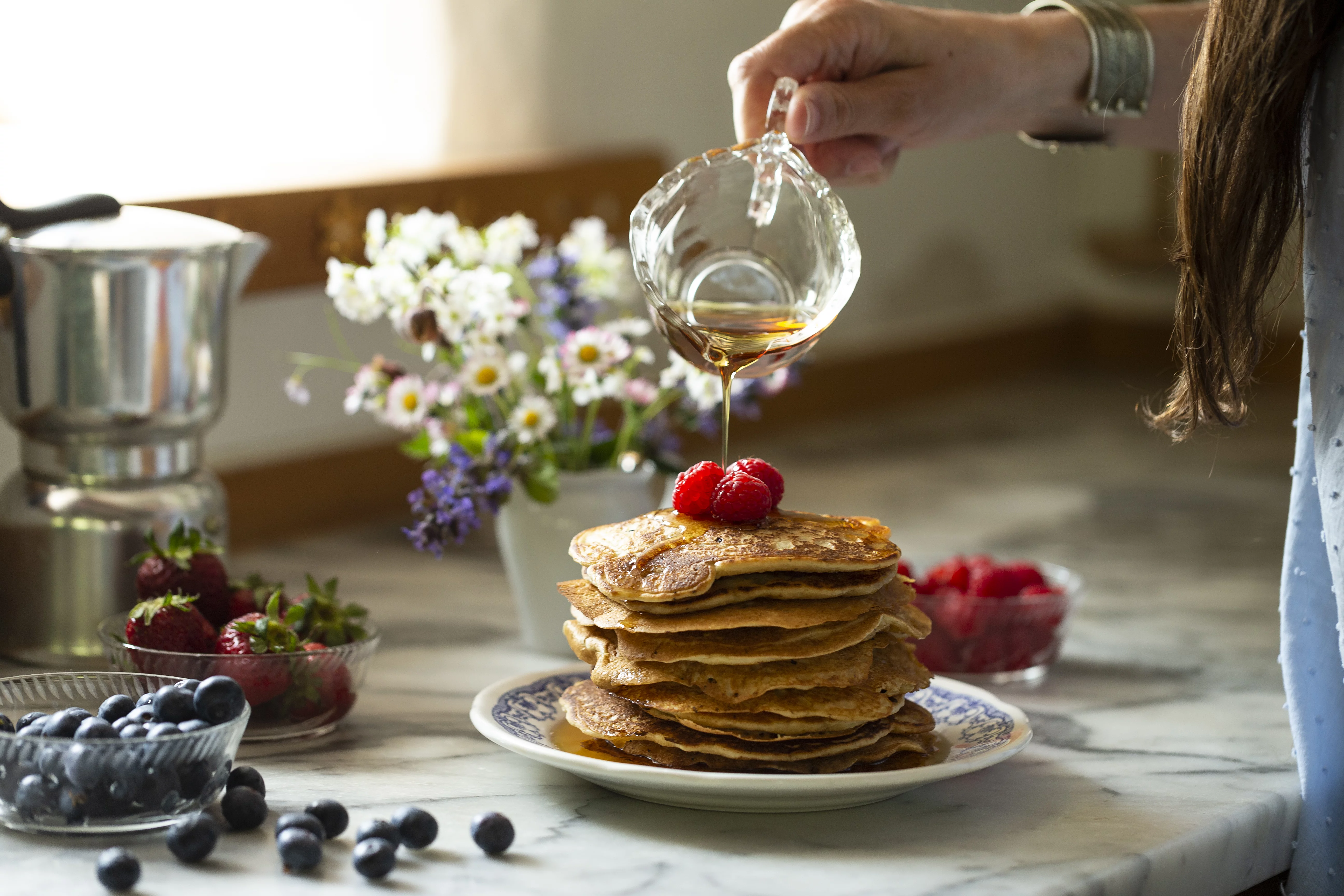 In idyllisch gestimmter Küchenatmosphäre werden frisch gebackene Pfannkuchen mit Ahornsirup übergossen
