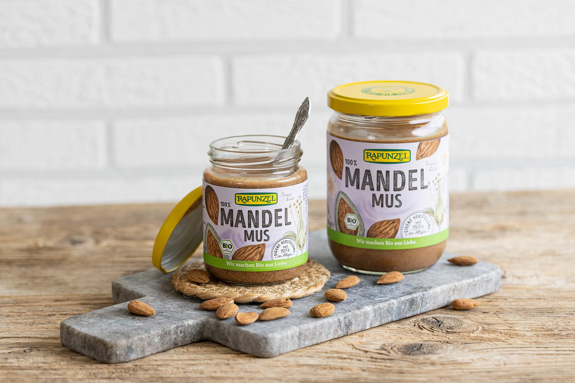 Zwei Gläser Rapunzel Mandelmus braun in unterschiedlichen Größen auf einem Marmorbrett – cremiges Bio-Nussmus aus 100 % Mandeln.