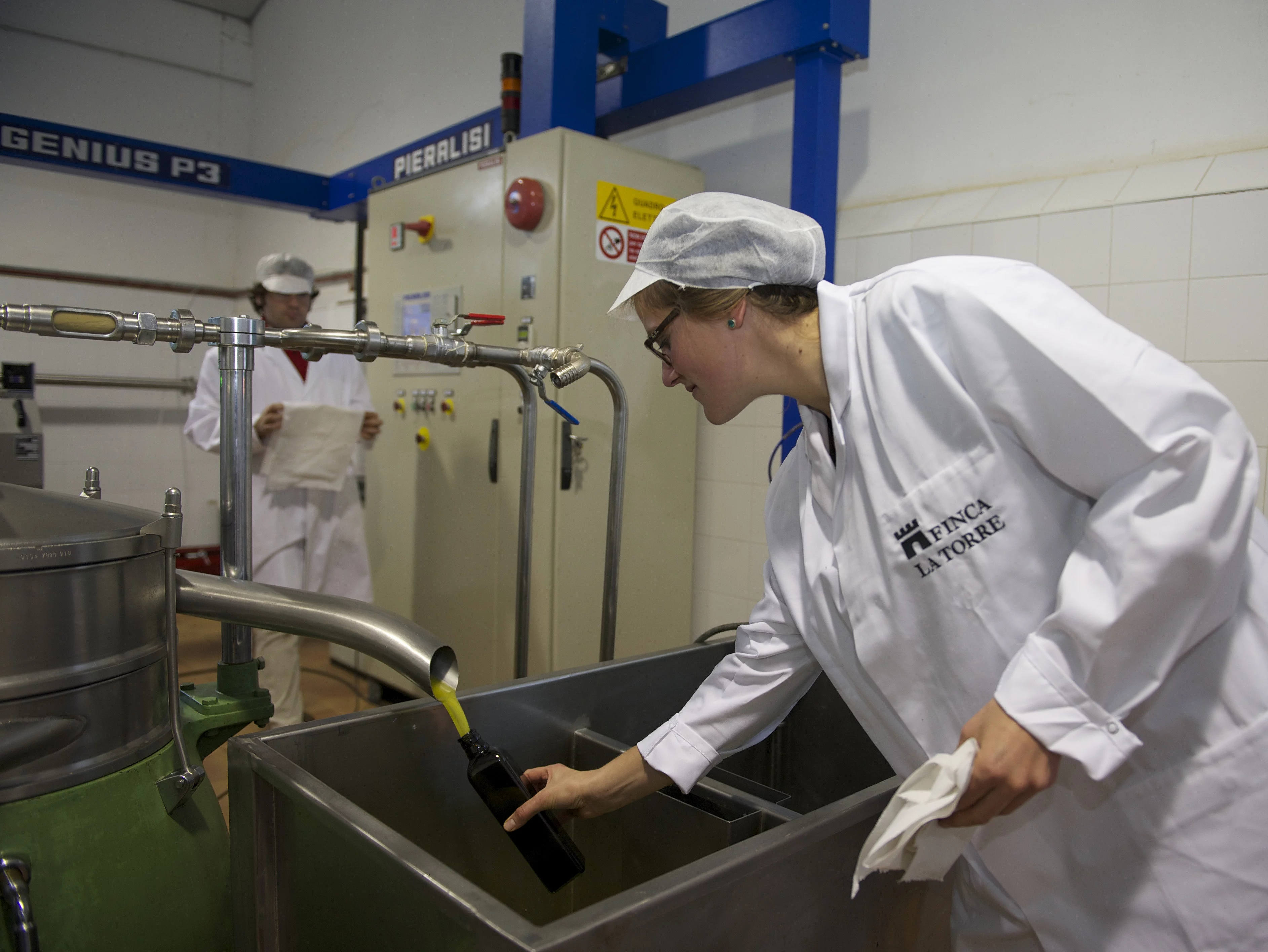Qualitätskontrolle bei der Olivenöl-Abfüllung. Eine Qualitätsmanagerin entnimmt eine Probe während der Olivenöl-Abfüllung in der Produktionshalle der Finca La Torre.