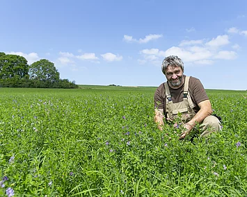 Haferbauer sitzt in Feld mit Grünland.