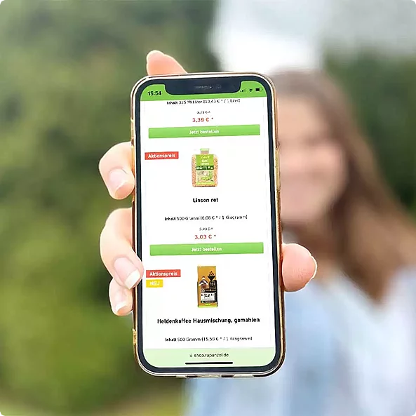 Mitarbeiter-Benefit von Rapunzel Frau hält Handy in die Kamera, auf dem Display sieht man Rapunzel Produkte im Rapunzel Webshop.