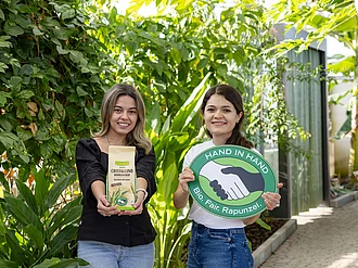 Die Leiterinnen des HAND IN HAND-Partners Manduvira mit Zuckerrohr, einer Packung Rohrzucker und dem HAND IN HAND-Logo.