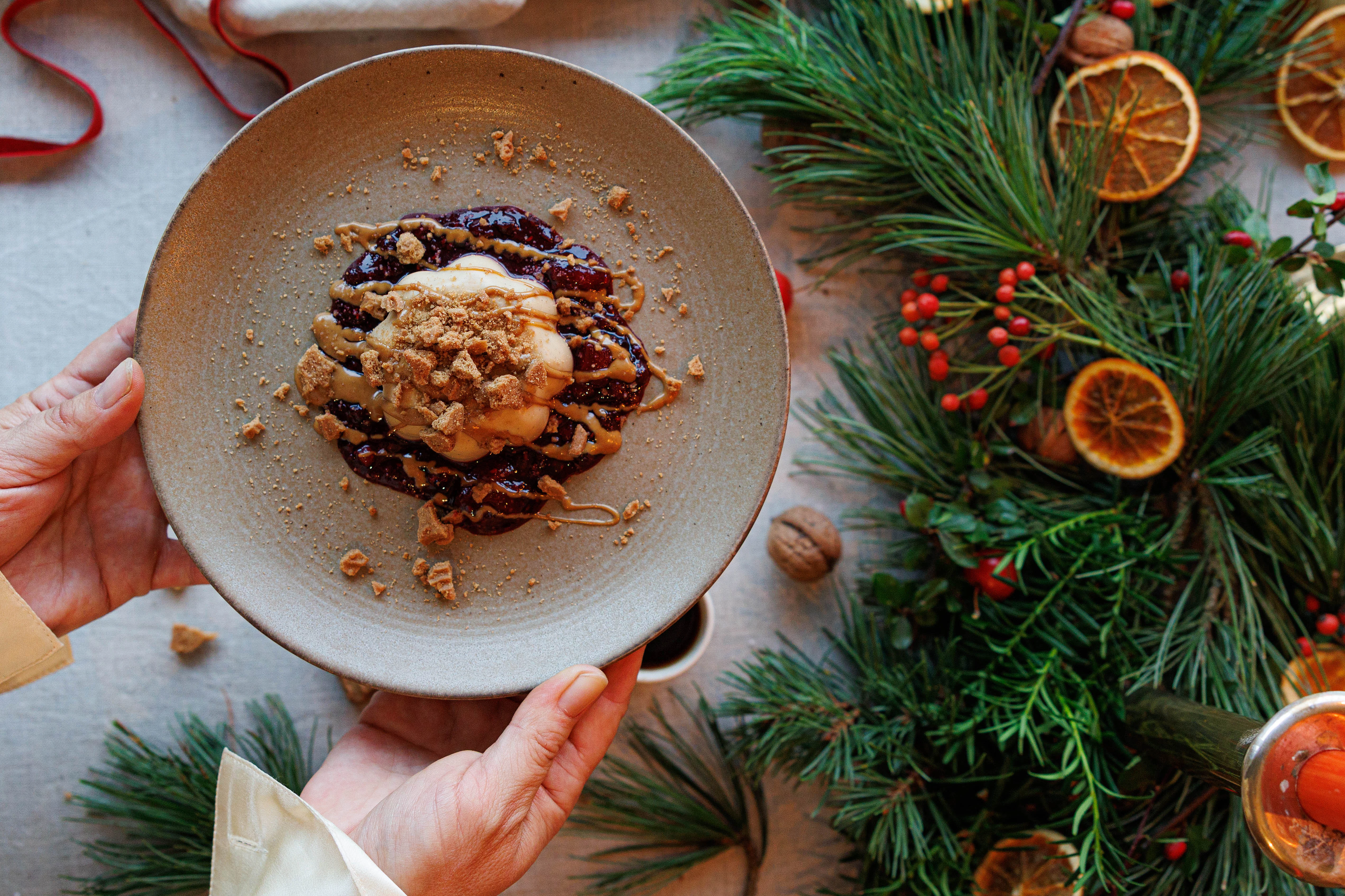 Spekulatius-Panna-Cotta mit Beerensauce, angerichtet auf Teller neben weihnachtlichem Tannengrün mit getrockneten Orangenscheiben.