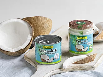 Kokosmilch und Kokosöl von Rapunzel auf Brett neben Kokosnuss.