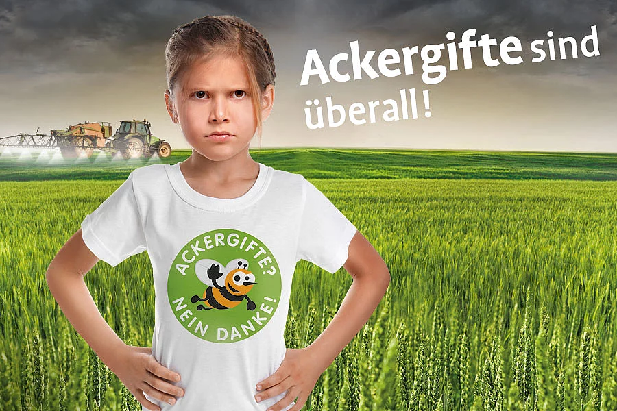 Auf dem Kampagnenbild, zu Ackergifte? Nein Danke! steht ein verärgertes Mädchen auf einem Feld, auf dem im Hintergrunde ein Pestizid versprühender Traktor im Einsatz ist.