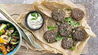 Mehrere Quinoabratlinge auf Backpapier, daneben ein cremiger Dipp und Gemüse. 