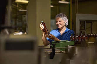 Rapunzel Mitarbeiterin hält eine Flasche Bio-Olivenöl ins Licht zur Qualitätskontrolle in der Produktion.