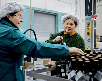 Zwei Frauen in Arbeitskleidung beim Abpacken der fertig abgefüllten Balsamico-Flaschen.