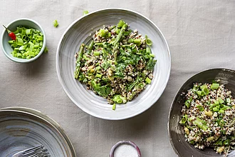 Spargelsalat mit buntem Quinoa und Edamame Sojabohnen in grau-blauem Teller auf Tischdecke.