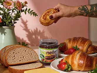 bionella Glas auf fancy Frühstückstisch bionella Glas auf Frühstückstisch mit Butter und Brötschen mit rosa Hintergrund