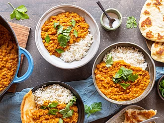 Linsen Dal und Himalaya Basmati Reis weiß, angerichtet in drei Tellern, daneben Naan.