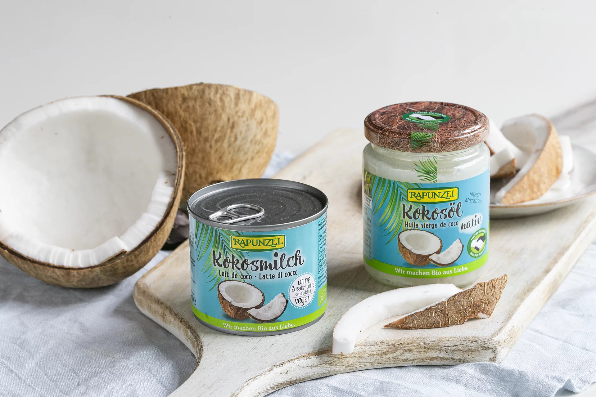 Kokosmilch und Kokosöl sind nur zwei der vielen Kokosprodukte von Rapunzel. Kokosmilch und Kokosöl von Rapunzel auf Brett neben Kokosnuss.