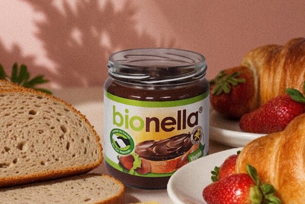 Gedeckter Tisch mit bionella, Butter, Brot, Croissants. In der Hand ein Croissants.  