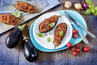 Zwei Auberginen-Hälften, die mit Lupinenschrot gefüllt sind und auf einem Teller angerichtet sind.