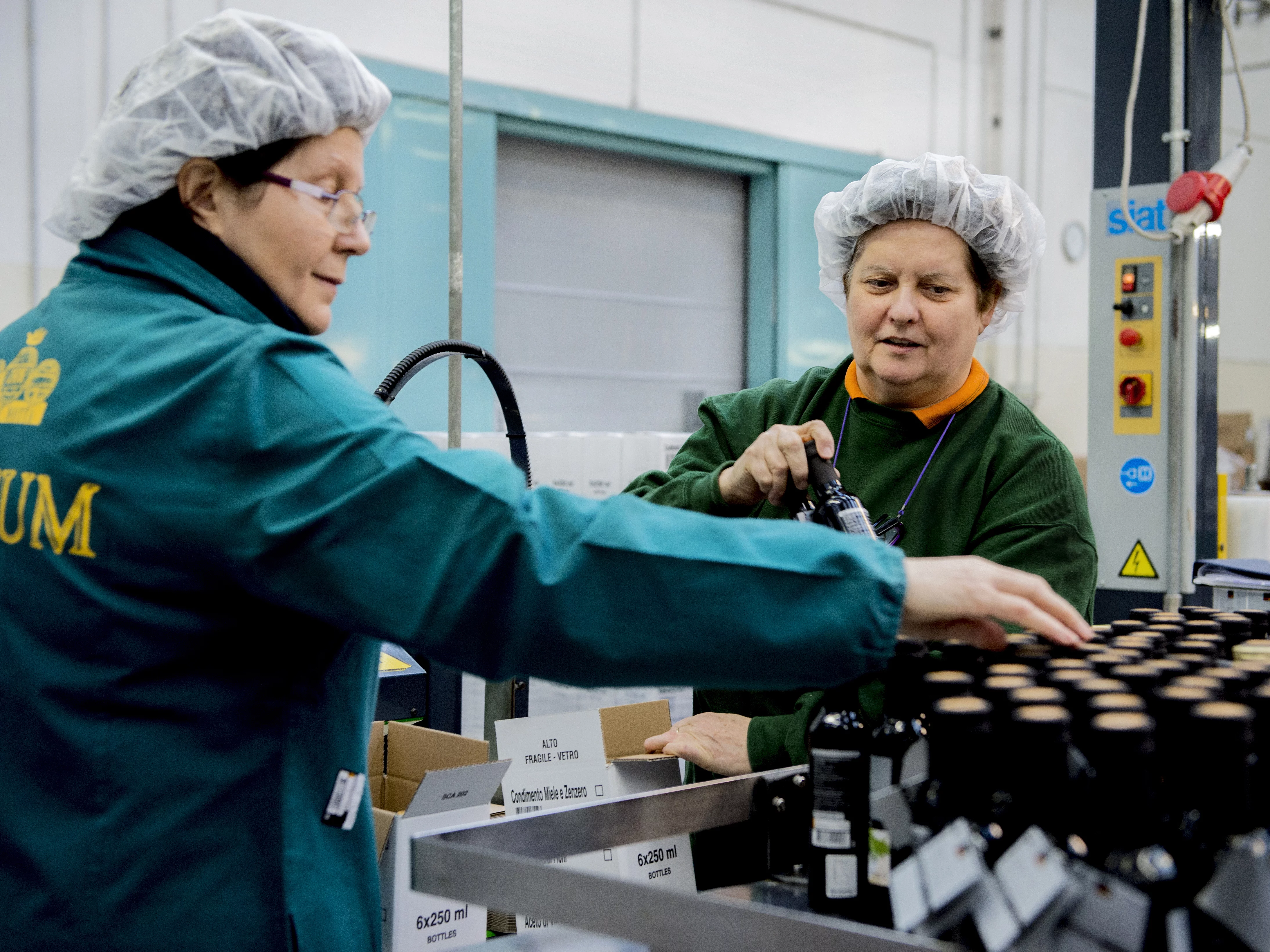 Zwei Frauen in Arbeitskleidung beim Abpacken der fertig abgefüllten Balsamico-Flaschen.