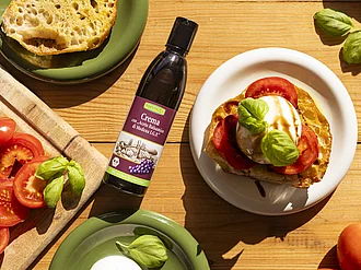 Baguette mit Burrata und Tomate neben einer Flasche Rapunzel Crema con 'Aceto Balsamico di Modena I.G.P.'