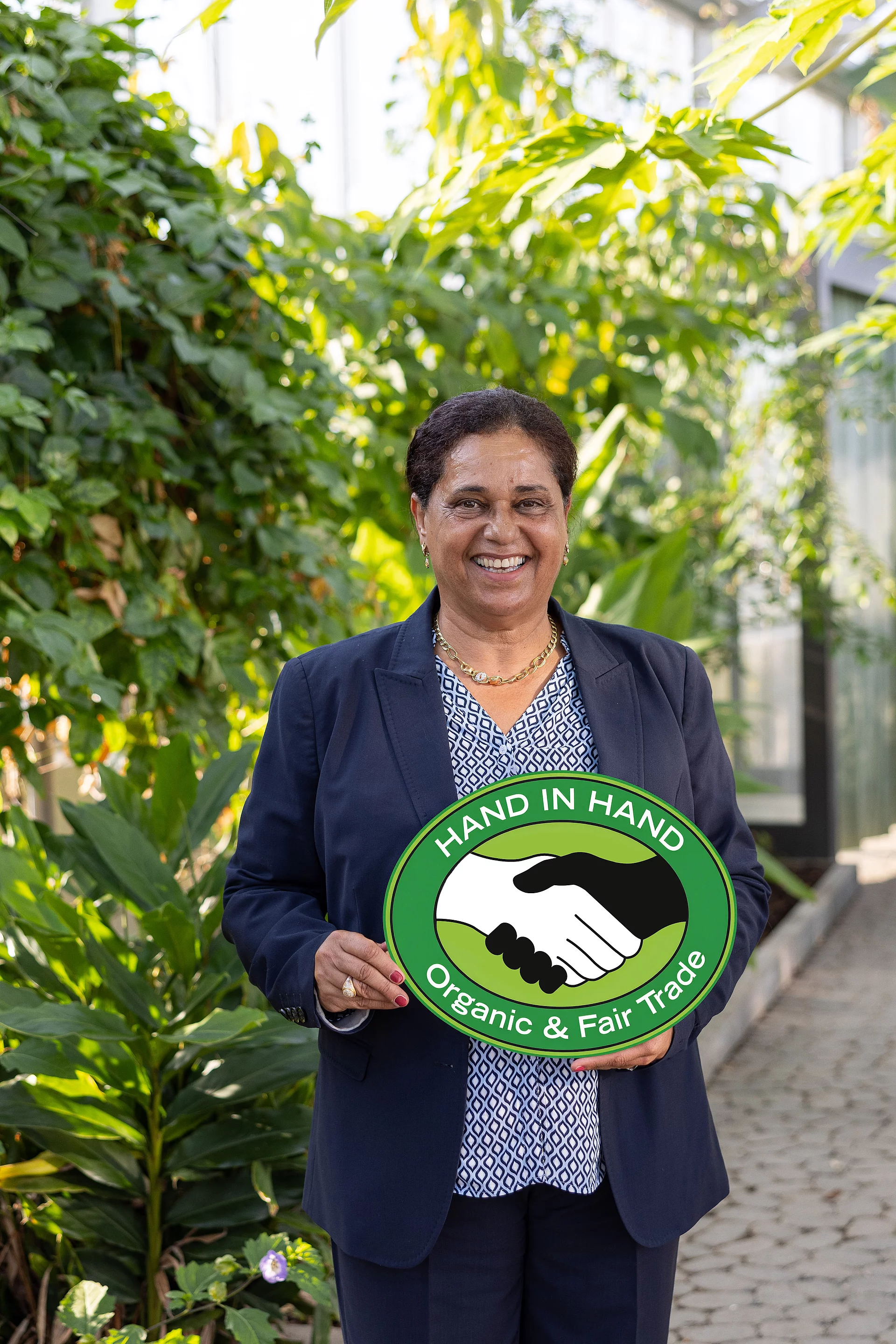 Gründerin Samia Chibani zu Besuch bei Rapunzel in Legau. Firmengründerin Samia Chibani mit einem HAND IN HAND-Schild im Tropenhaus bei Rapunzel in Legau.