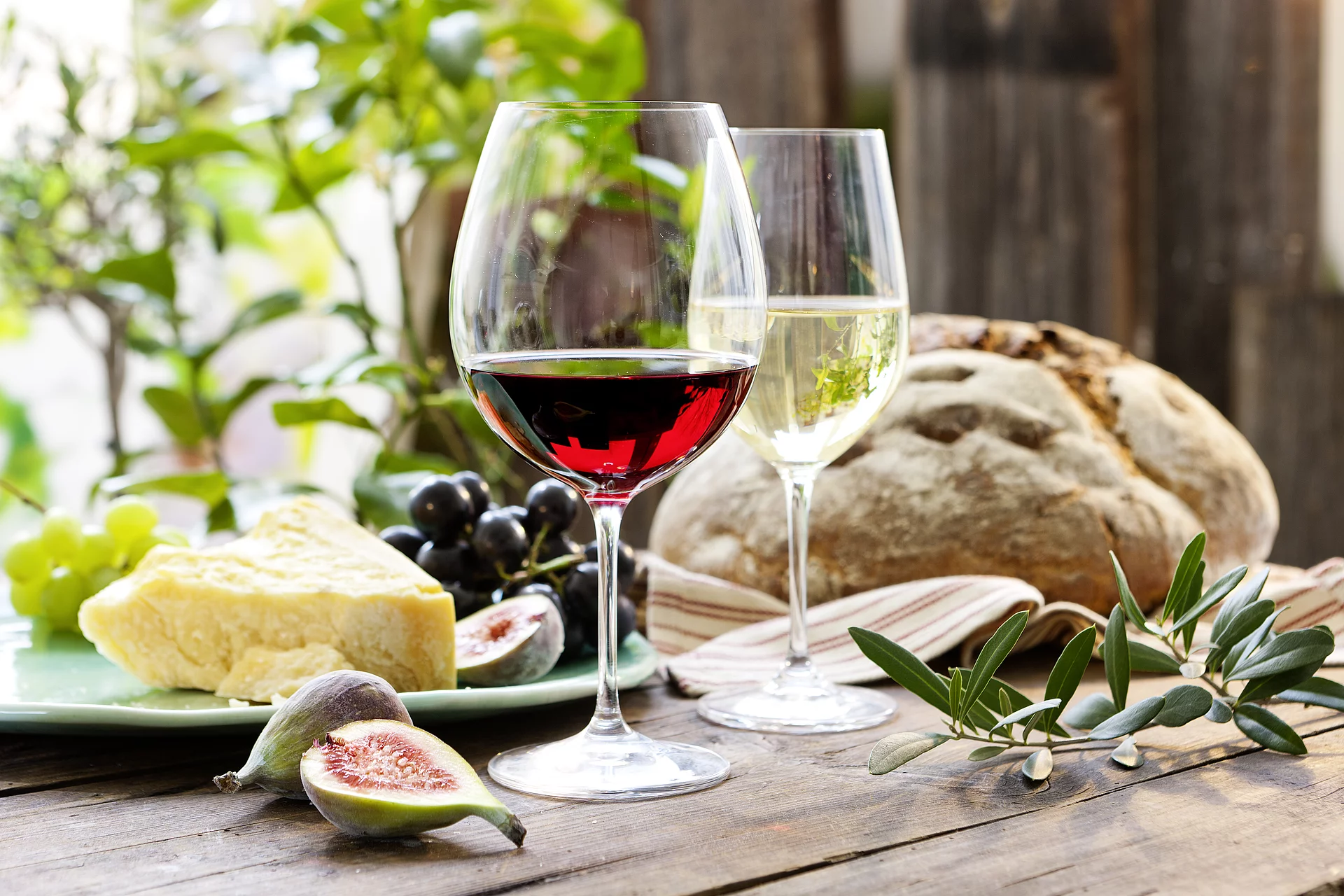 Rotwein steht für Tiefe, Wärme und Genuss. Gefülltes Rotweinglas vor Weißweinglas, daneben Käse und Brot.