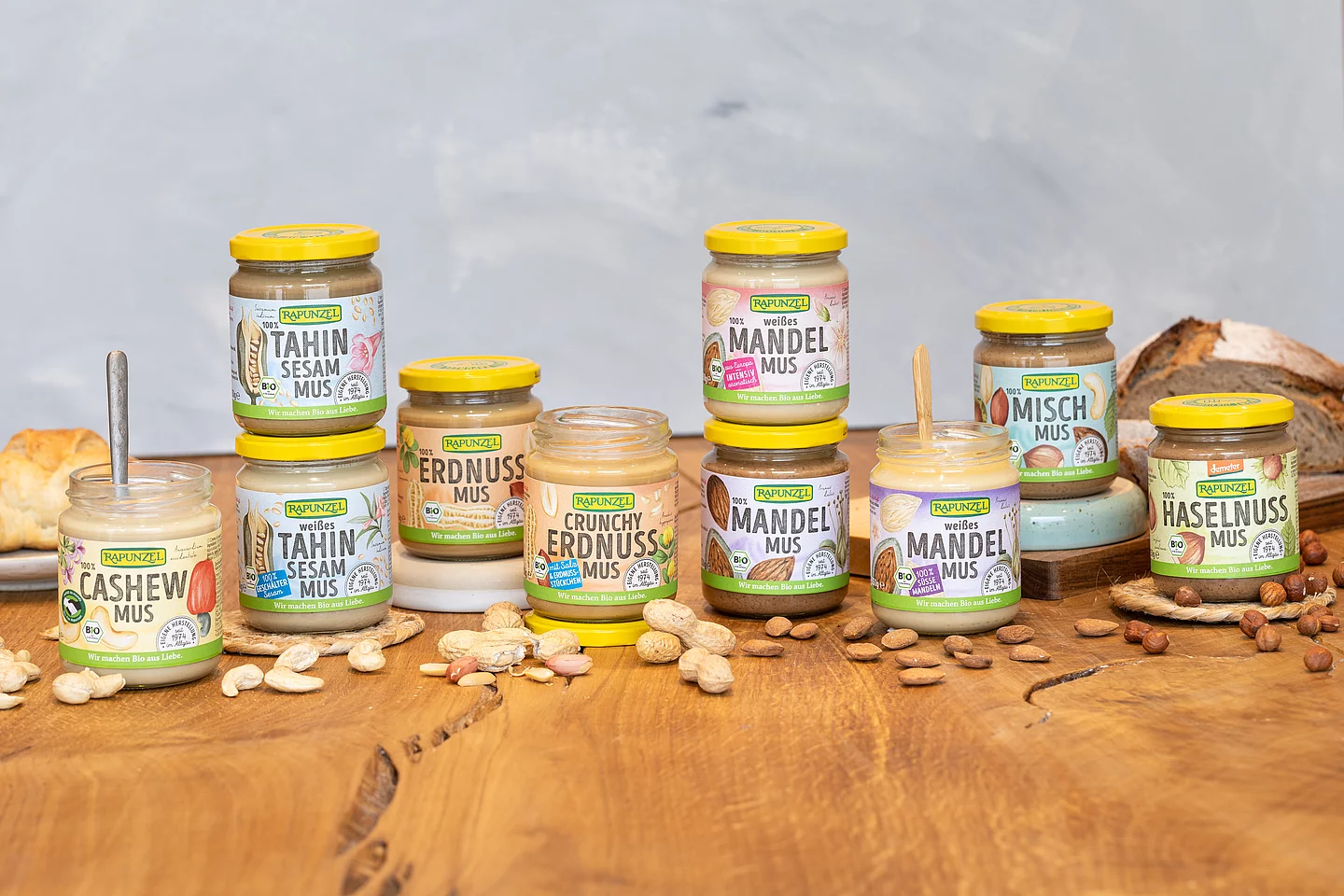 Rapunzel Nussmuse in Bio-Qualität auf einem Holztisch, im Hintergrund ein Laib Brot – cremige Muse aus 100 % Nuss, ideal für Brotaufstrich und kreative Küche.
