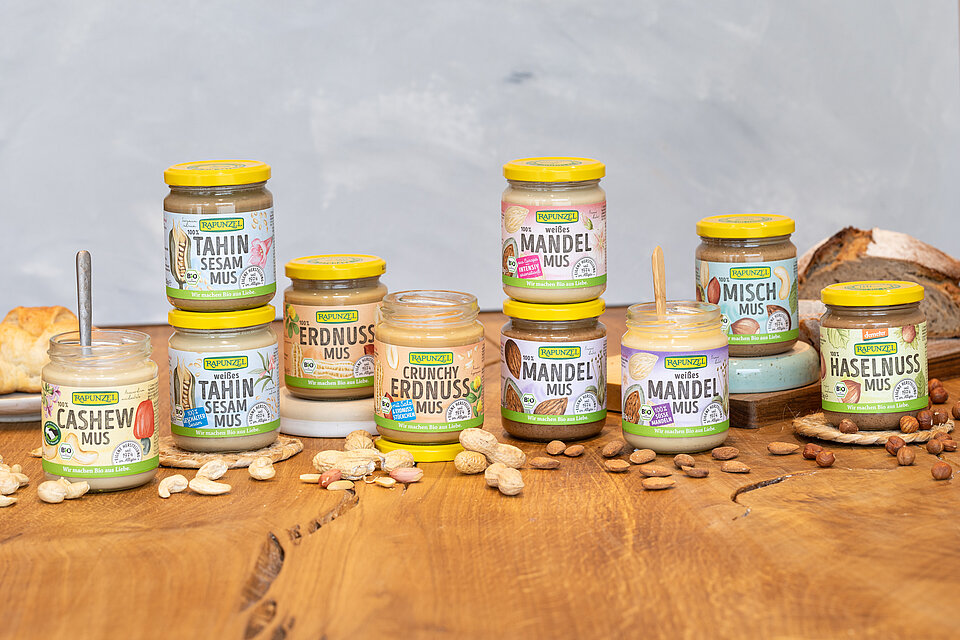 Rapunzel Nussmuse – 100 % Nuss, Bio-Qualität und Vielfalt für deine Rezepte. Rapunzel Nussmuse in Bio-Qualität auf einem Holztisch, im Hintergrund ein Laib Brot – cremige Muse aus 100 % Nuss, ideal für Brotaufstrich und kreative Küche.
