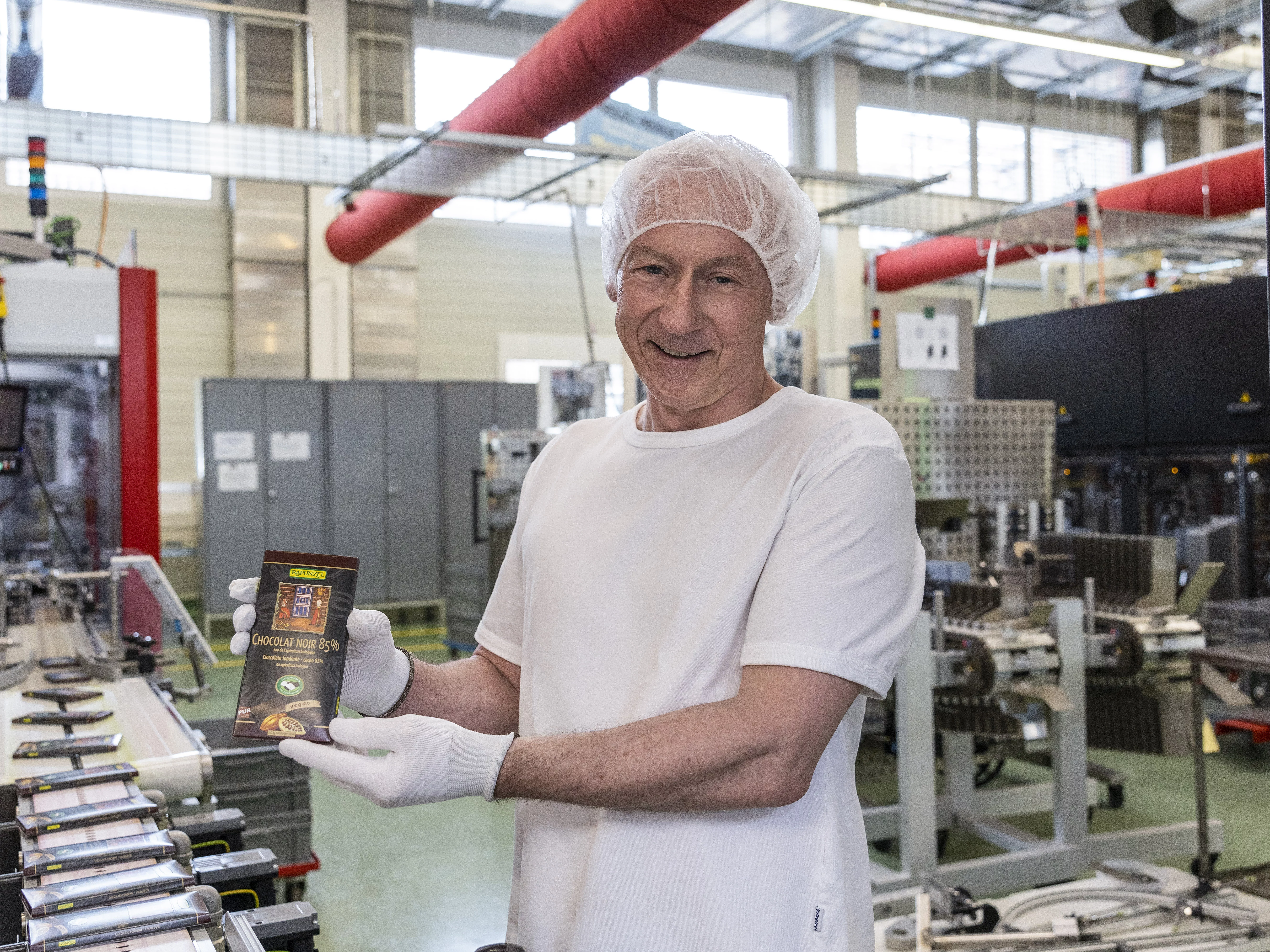 Produktionsmitarbeiter hält stolz eine Tafel Rapunzel Schokolade in die Kamera.