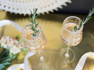 Rapunzel Prosecco mit Rosmarin-Stengel im Glas auf tisch in festlicher Atmosphäre