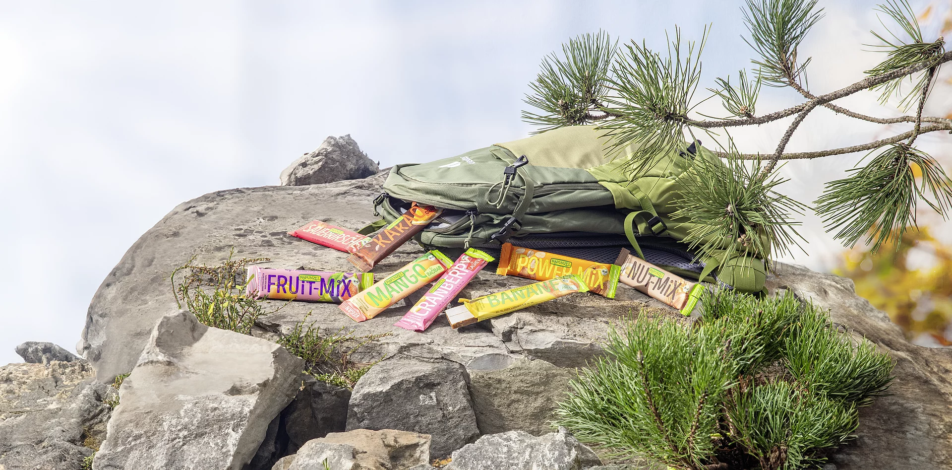 Auf einem Felsen liegt ein Wanderrucksack, aus dem Rapunzel Fruchtschnitten herausgefallen sind.