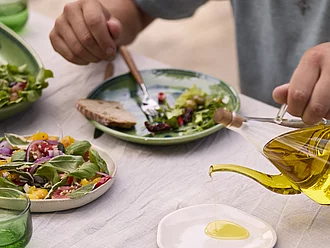Tisch mit frischen Salatvariationen, Tomaten-Mozzarella und Olivenöl-Dekantierer – Rapunzel Bio-Olivenöl für mediterrane Küche