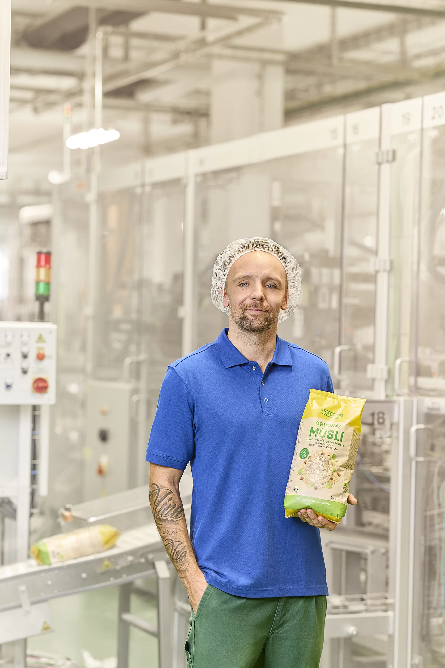 Mitarbeiter aus der Produktion steht neben der Abpackmaschine und präsentiert fertig abgepacktes Müsli.