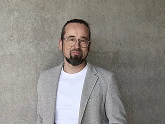 Rapunzel Geschäftsführer Werner Berlage steht lässig an eine Betonwand gelehnt und schaut freundlich in die Kamera