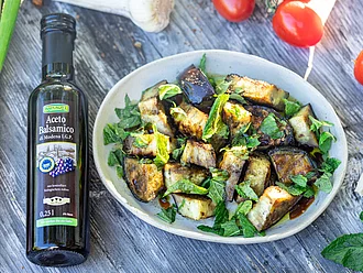 Teller mit marinierten Auberginen, Balsamico-Flasche liegt daneben.