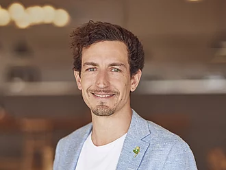 Porträt von Leonhard Wilhelm. Er ist Geschäftsleitung und Gesellschafter. Das Foto zeigt ihn frontal, lächelnd und formell gekleidet. Der Hintergrund ist unscharf.