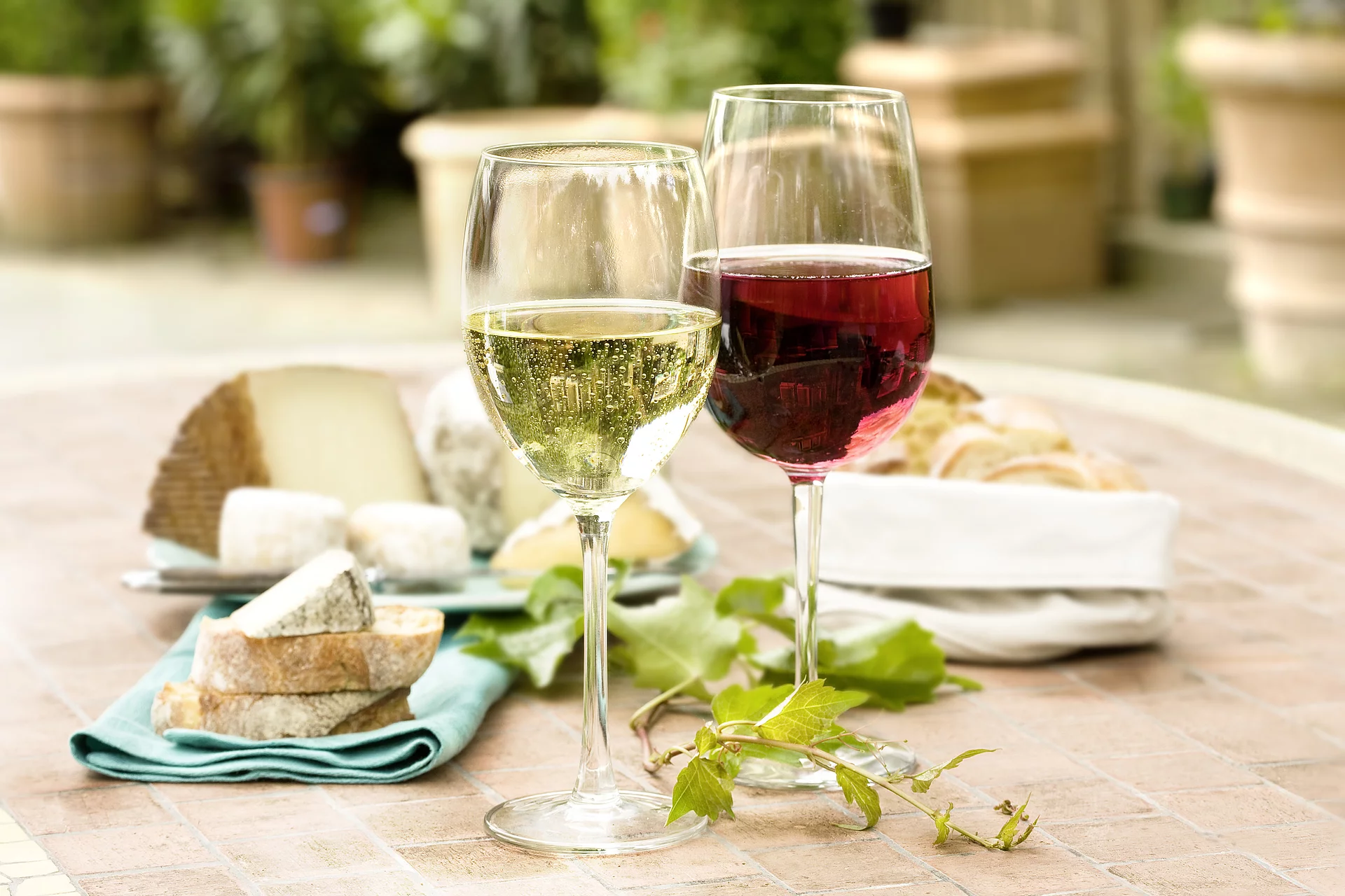 Weißwein schmeckt frisch. Weißweinglas neben Rotweinglas, dahinter Käse und Brot.