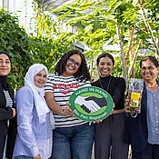 Gruppenfoto im Tropenhaus von Rapunzel mit CCF-Gründerin Samia Chibani. Mit im Bild sind das HAND IN HAND-Logo und die Datteln, die von Rapunzel verkauft werden.