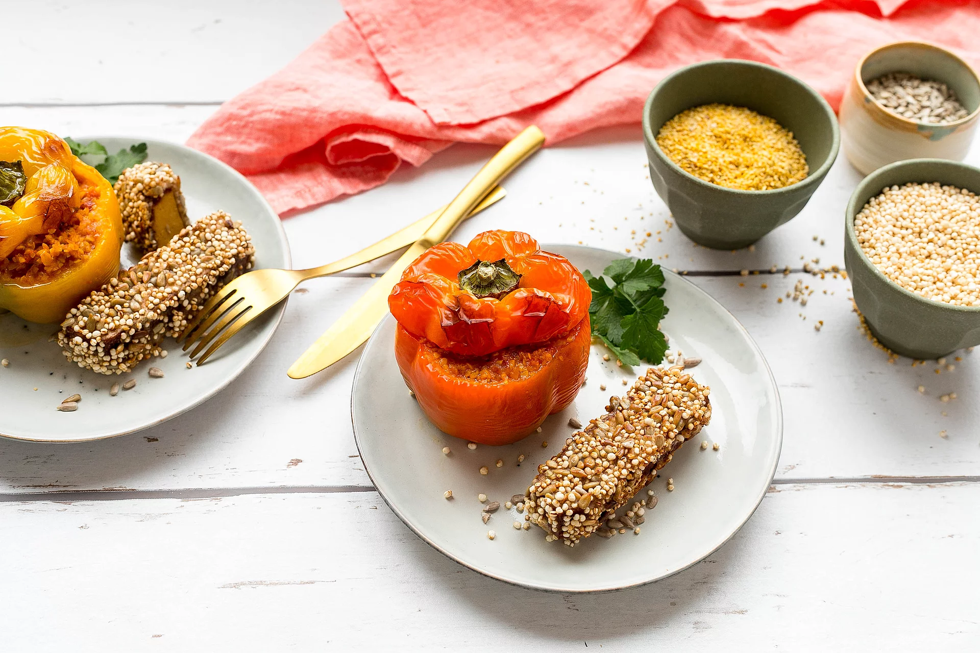 Gefüllte Lupinen-Paprika mit Räuchertofu mit Quinoa-Kruste. Mit Lupinenschrot gefüllte gelbe und orangene Paprika mit Räuchertofu auf Tellern angerichtet.