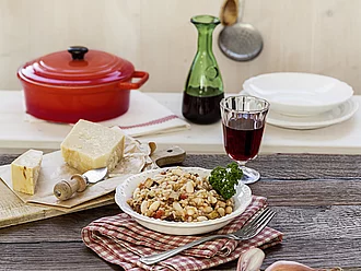 Teller mit Risotto, daneben Käse, Zwiebel, Rotwein, Topf.