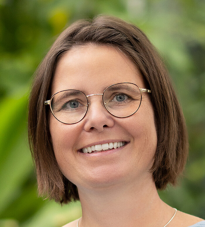 Rapunzel Mitarbeiterin steht vor blühender Pflanze.